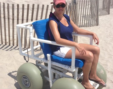 A woman sits in a PVC Beach Wheelchair on a sandy beach