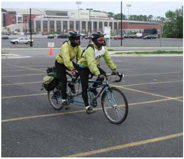 Figure 4: Photo. Tandem bicycle. Two adults are riding a tandem bicycle in a parking lot.