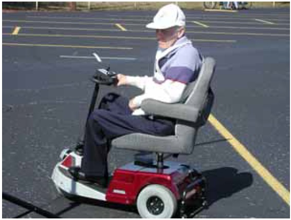 Figure 10: Photo. Assistive powered scooter. A man is in an assistive powered scooter in a parking lot.