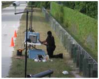 Figure 23: Photos. Equipment testing at data collection stations. This is a mosaic of five photos. 
Photo 23e: An event staff person checking equipment alongside the trail.