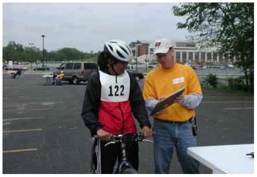 Figure 30: Photo. The participants were briefed at the turning radius station. An event staff person is briefing a participant on a bicycle.