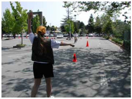 Figure 31: Photo. Research staff oversaw the turning radius station to ensure proper participant flow-through. A participant on a bicycle is riding through a turning path. An event staff person is watching him and directing him toward the next turning path. 
