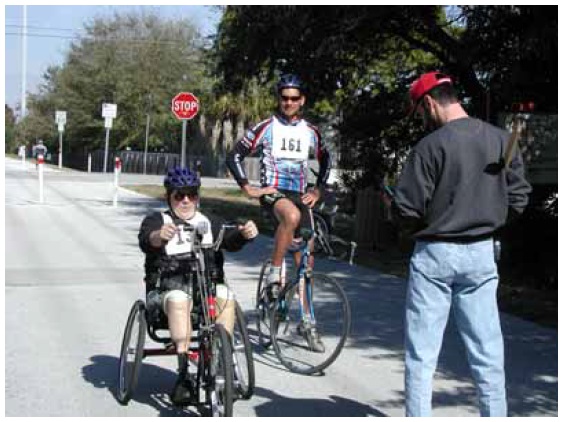 Figure 35: Photo. Participants were asked to accelerate to their normal speed. An event staff person is instructing two participants - one on a bicycle and one on a hand cycle - at the acceleration station.