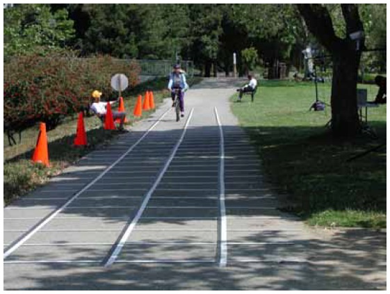 Figure 42: Photo. STOP sign controller signaling a bicyclist to stop. A participant is riding her bicycle through the stopping sight distance section. An event staff person is holding up a STOP sign to signal the participant to stop 'as quickly as is comfortable.' 