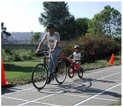 Figure 48: Photos. The longest users observed in this study exceeded 2.4 meters (8 feet) in length and should be considered the critical users.  Photo 48a: An adult participant is riding a bicycle and a child participant is riding a smaller, attached bicycle (a trailer bicycle).