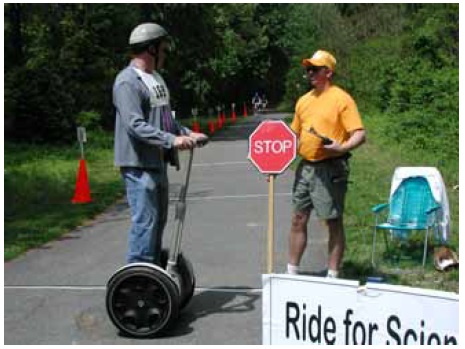 Figure 51: Photo. A Segway user on the Paint Branch Trail in Maryland. A participant standing on a Segway is talking to an event staff person.