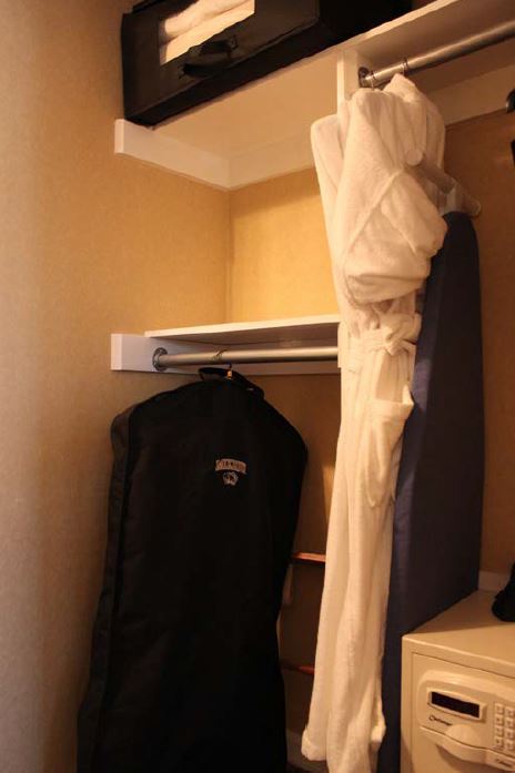 A bath rob and clothes hanging in a closet with an ironing board and safe