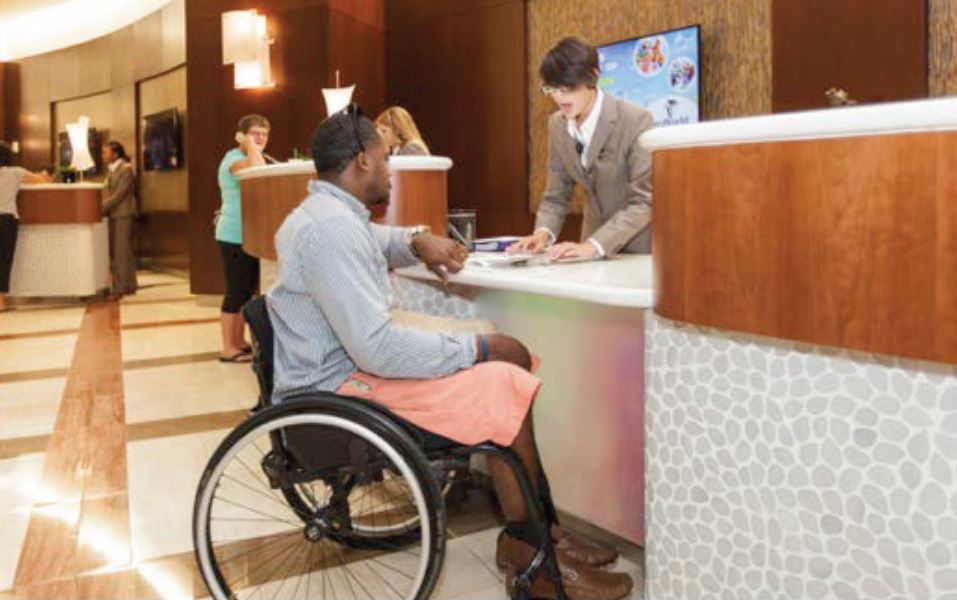 Man in a wheelchair checking in at a lowered hotel check in counter