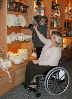 Museum shop interior where woman using wheelchair points out item for staff to retrieve