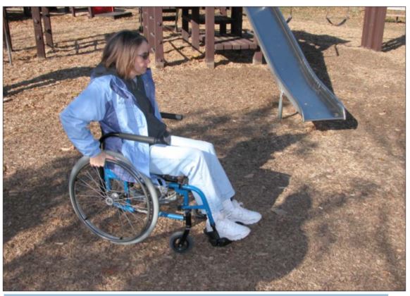 woman in wheelchair in playground setting that has an engineered wood product installed as the surface material