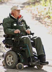 Photo of a man using a motorized wheelchair on a trail.