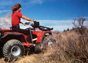 Photo of a woman riding an all-terrain vehicle in an area with tall grass.