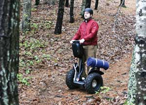 Photo of a man riding a Segway on a trail in a forest.