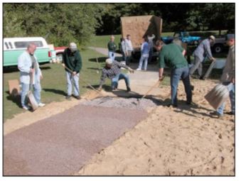 photo of a group of men using rakes to level the binder-ewf mixture near a junction with an asphalt path