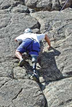 Photo of a man rock-climbing. The man is using a prosthetic leg.
