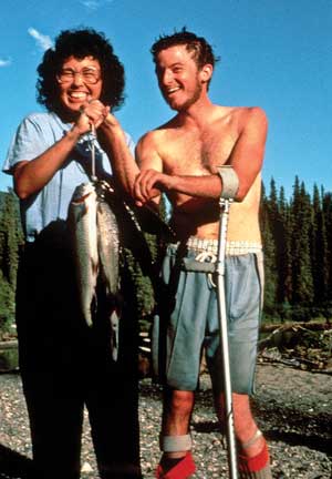 Photo of a woman and a man holding up a stringer of fish. The man is using metal balance supports that attach to his forearm near the elbow.