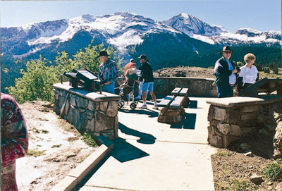 Photo of several people with and without disabilities, at a scenic overlook with mountainous vistas surrounding them.