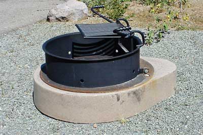 Photo of a manufactured steel fire ring mounted on a 9 inch (230 mm) high concrete base that is a few inches larger in diameter than the fire ring.