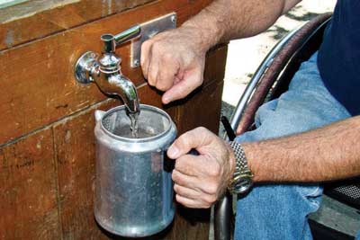 Photo of a man using his fist to depress a push button to dispense water into his coffee pot from a spigot.