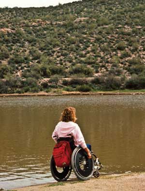 Photo of a woman using a wheelchair to travel along a lakefront beach.