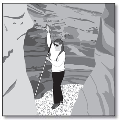 Photo of a woman with sunglasses and a cane in a slot canyon, using her free hand to search the top of the entrance to a cave in the side of the bedrock canyon wall.