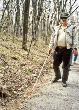 Photo of a man walking on a trail and using his cane to search the edge of the trail.