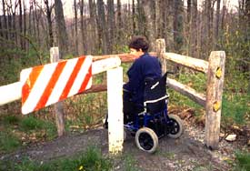 Photo of a woman in a wheelchair moving through a three-post passage around a gate