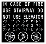 Sign that uses tactile letters, Braille and pictograms to convey the message "This way to the fire exit."