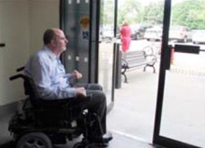 Man in a wheelchair at an office building - waiting at open sliding door