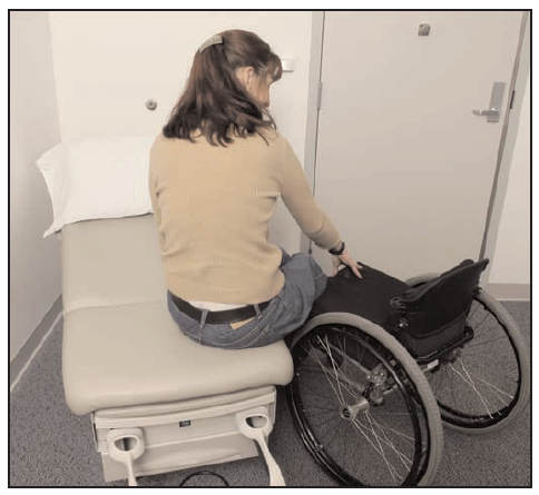 woman transferring from her wheelchair to a lowered exam table