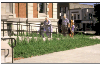 A photograph of the front of a historic town building with a ramp. An older woman using a walker is going up the ramp with a man and two children.
