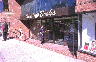 A front view of a store with an entrance that is below sidewalk level. Three steps lead down to the entrance. A sign is provided to direct customers to the accessible entrance.