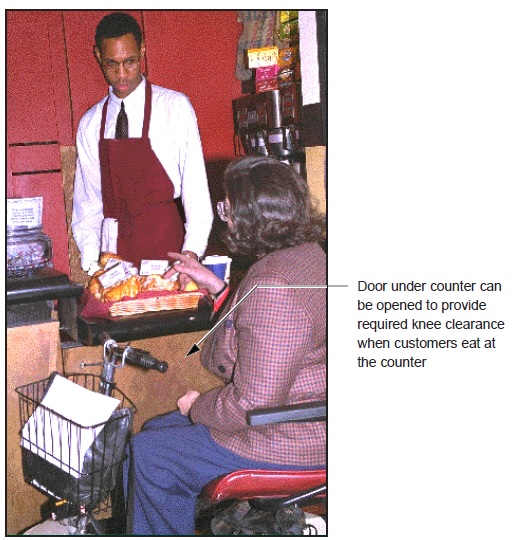 photo - staff serving items on a lowered counter. note: Door under counter can be opened to provide required knee clearance when customers eat at the counter.