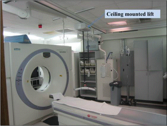 Photo of a CT room shown the CT equipment and an overhead lift mounted on the ceiling.