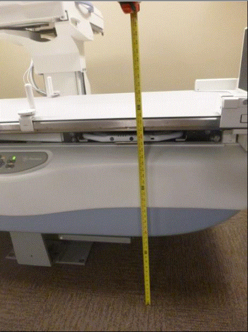 Picture of an Angulating Radiographic and Fluoroscopic Exam Table whose fixed height is approximately 34.5 inches. Tape measure shown beside transfer surface to show height. Also note the equipment imaging components on the opposite side of where the patient transfers.