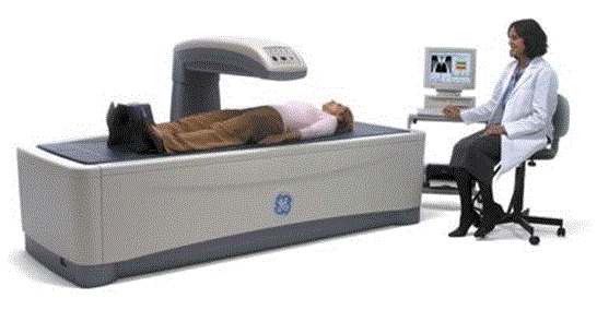 Picture shows a Dual Energy X-ray Absorptiometry (DXA) system for Osteoporosis assessment with a patient lying on the scanning bed. A technician is seated beside the equipment viewing a computer monitor. 