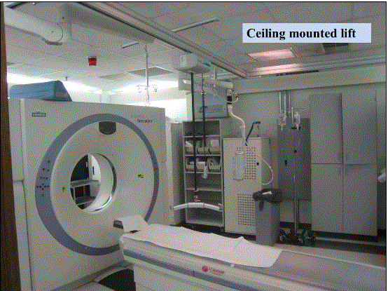 Photo of a CT room shown the CT equipment and an overhead lift mounted on the ceiling.