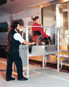A woman in a wheelchair boards a train via a lift being operated by a man