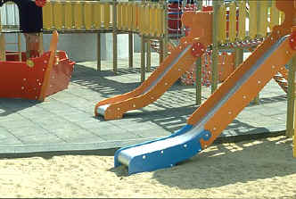 photo of 2 slides with one connected by an accessible route and the other by inaccessible surfacing (sand)